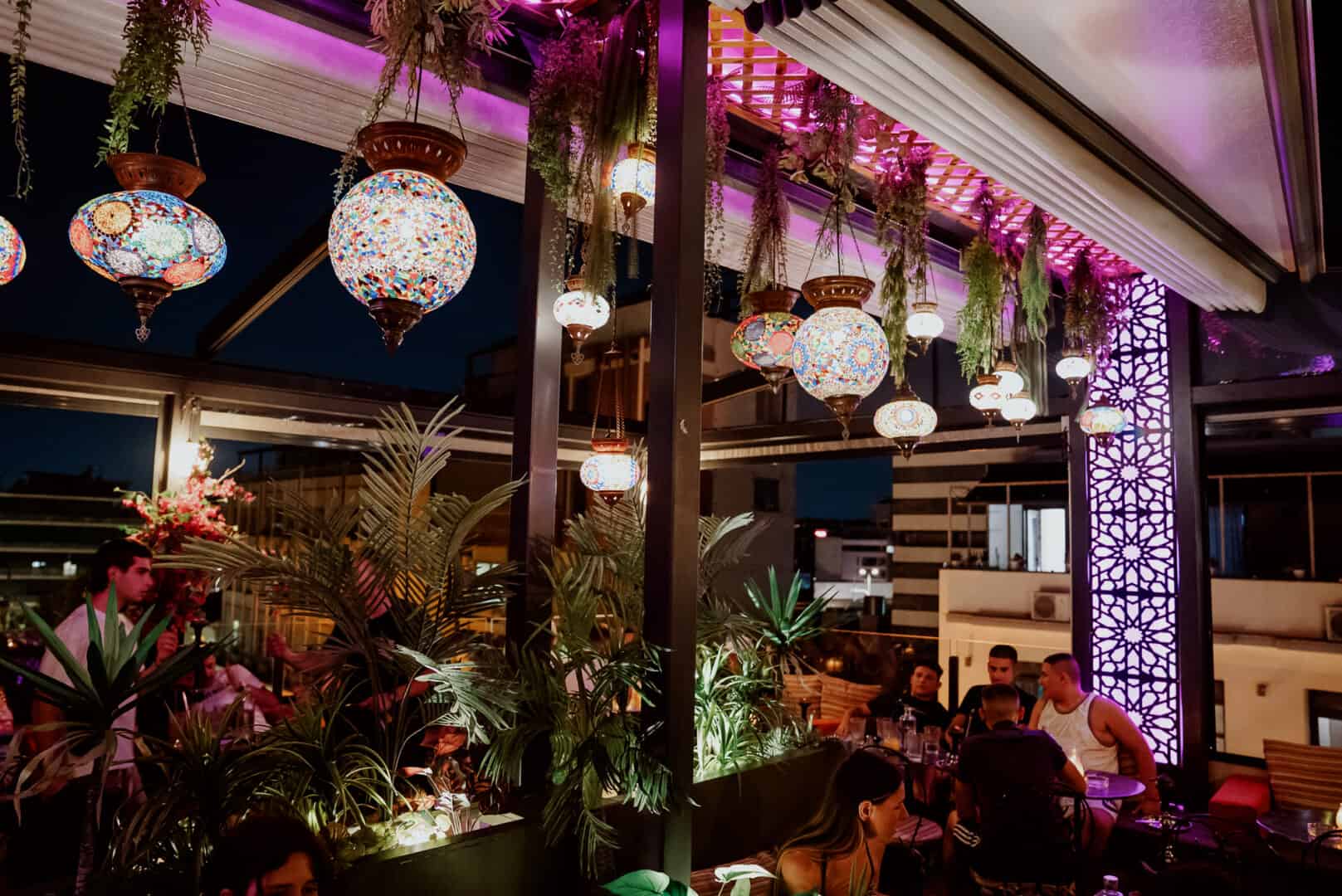 Vibrant hookah lounge with colorful hanging lamps and lush greenery.